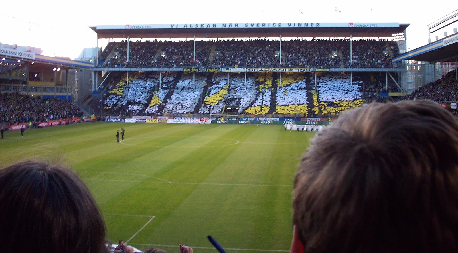 AIK-supportrar håller upp svarta, vita och gula ark i ett mosaiktifo på Råsundas läktare före derbyt mot Djurgården 2008.
